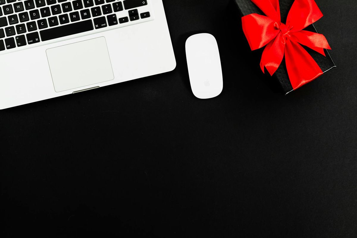 Flat lay of laptop and gift box with red bow on black background. Ideal for online shopping or gift themes.