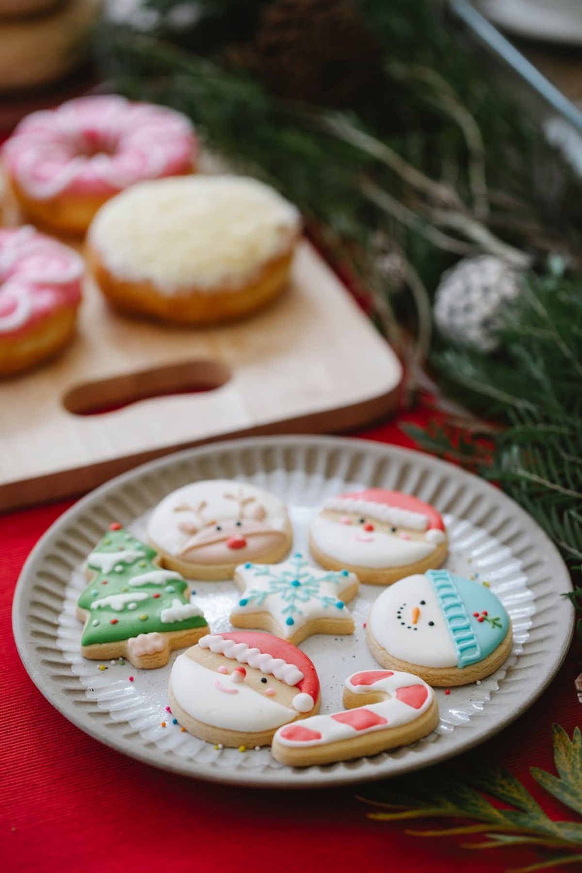 From above table decorated with coniferous branches and sweet gingerbread served on wooden board near glazed Christmas cookies on ceramic plate
