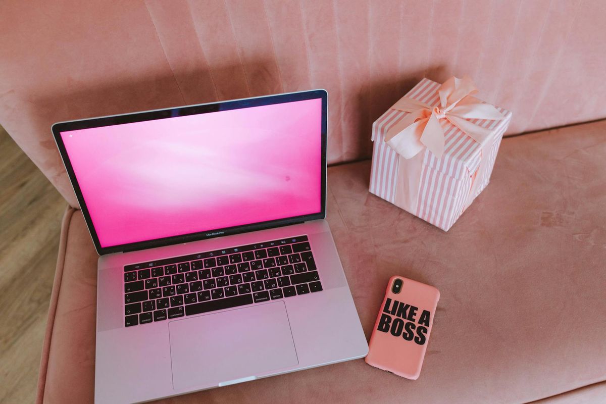 A modern workspace featuring a pink-themed laptop, a gift box, and a phone on a pink sofa.