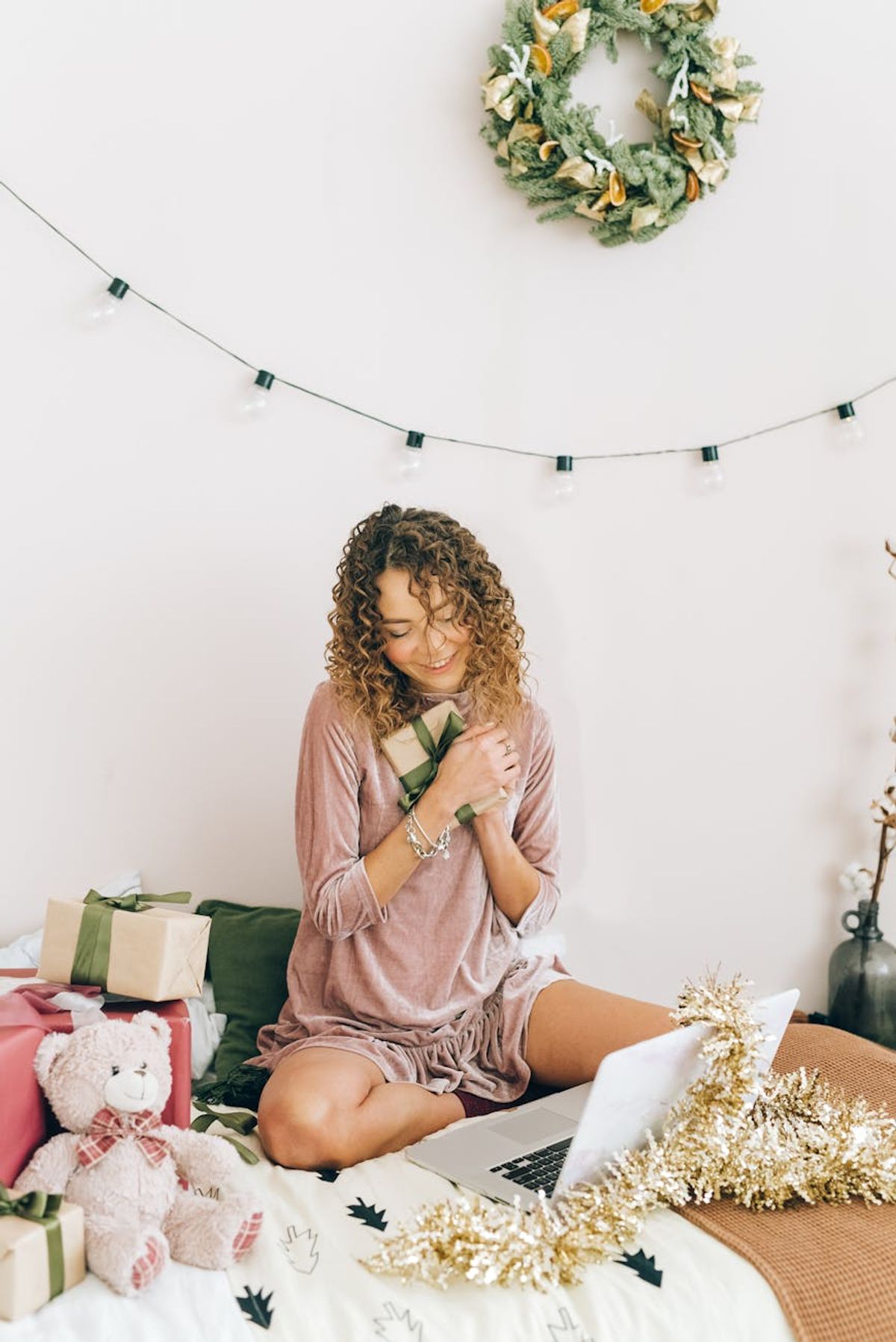 Smiling woman sitting with Christmas gifts and laptop, enjoying holiday moments indoors.