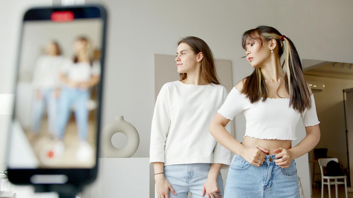 Two women recording dance moves on a smartphone indoors, showcasing lifestyle creativity.