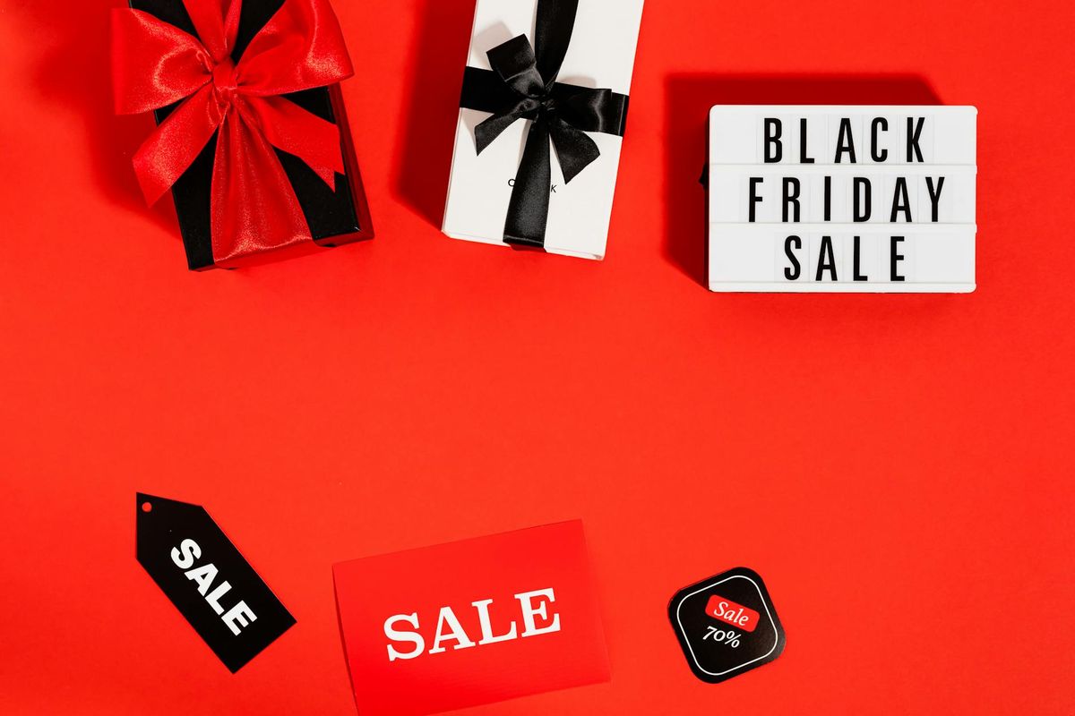 Bright flat lay featuring Black Friday sale items, gift boxes with bows, and sale tags on red background.