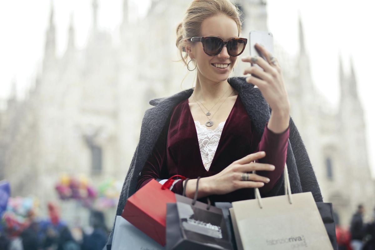 Stylish woman with shopping bags takes a selfie near Milan's famous Duomo on a bright day.