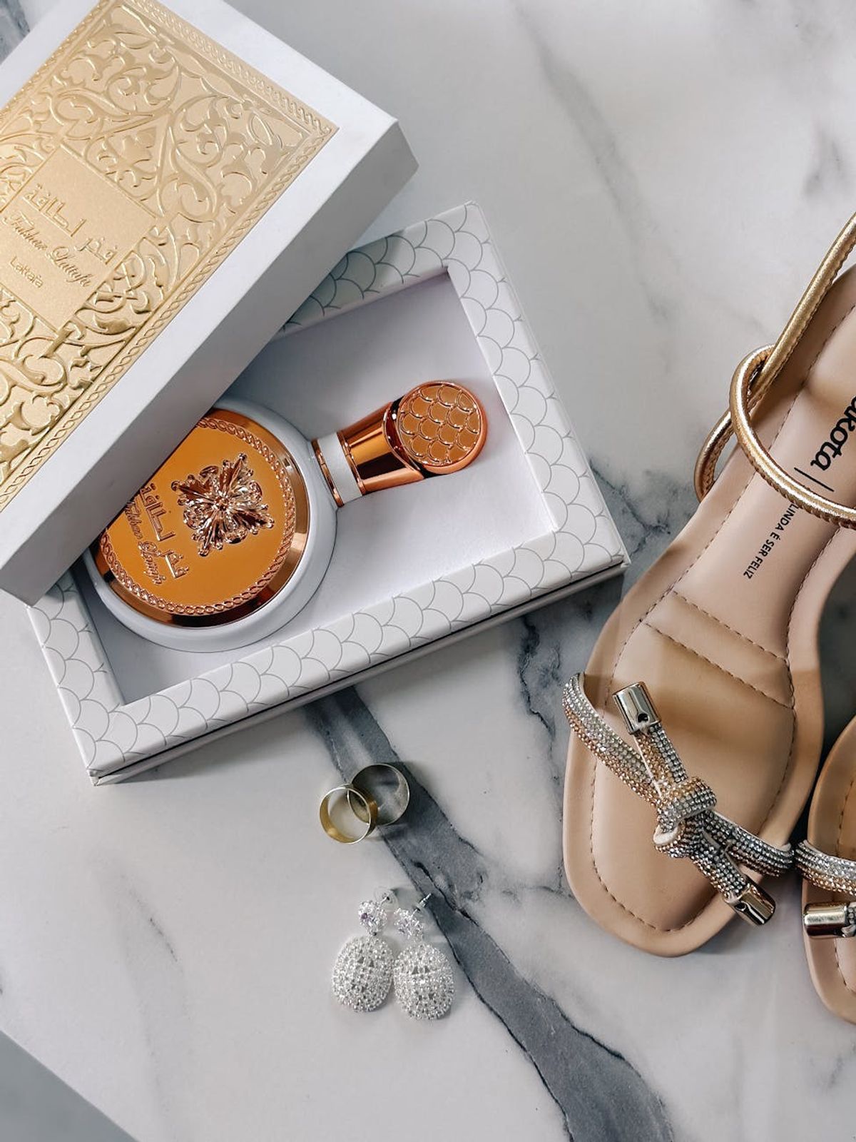 An arrangement of luxury accessories including perfume, shoes, and jewelry on a marble background.