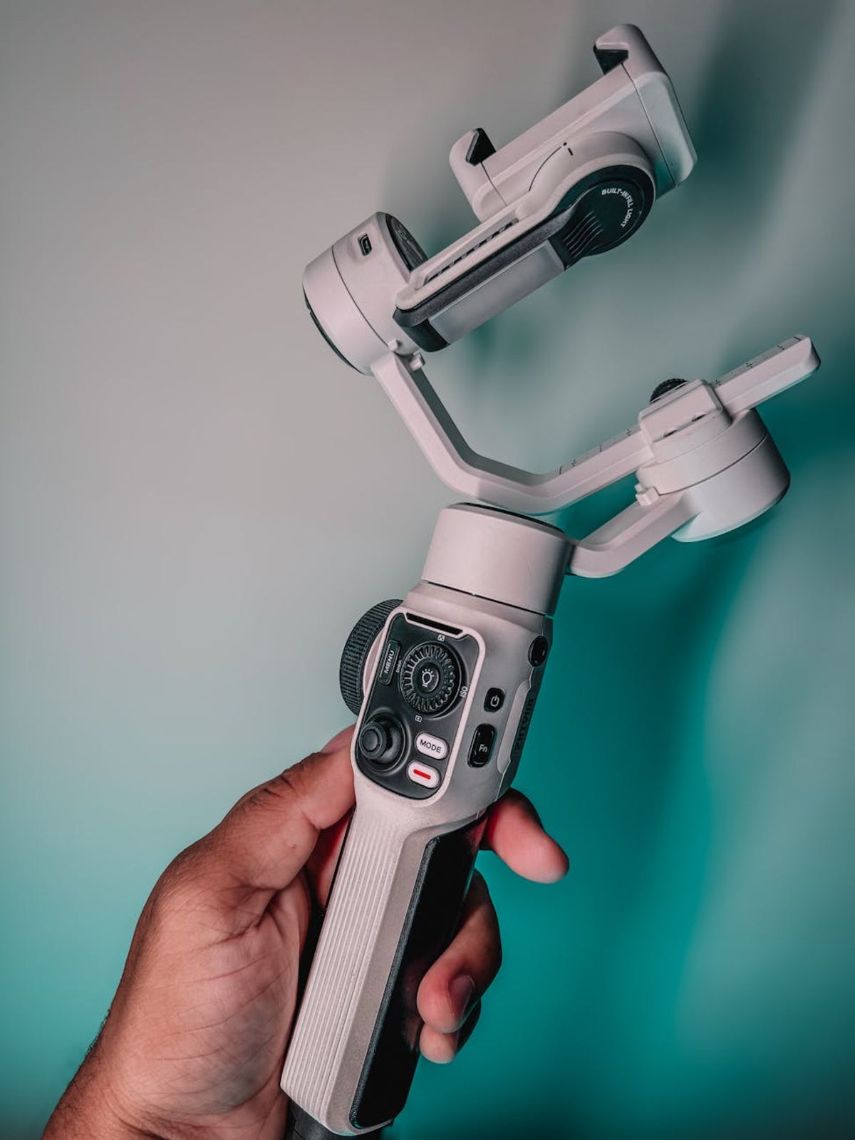 A person holding a gimbal stabilizer for mobile photography in a studio setting.