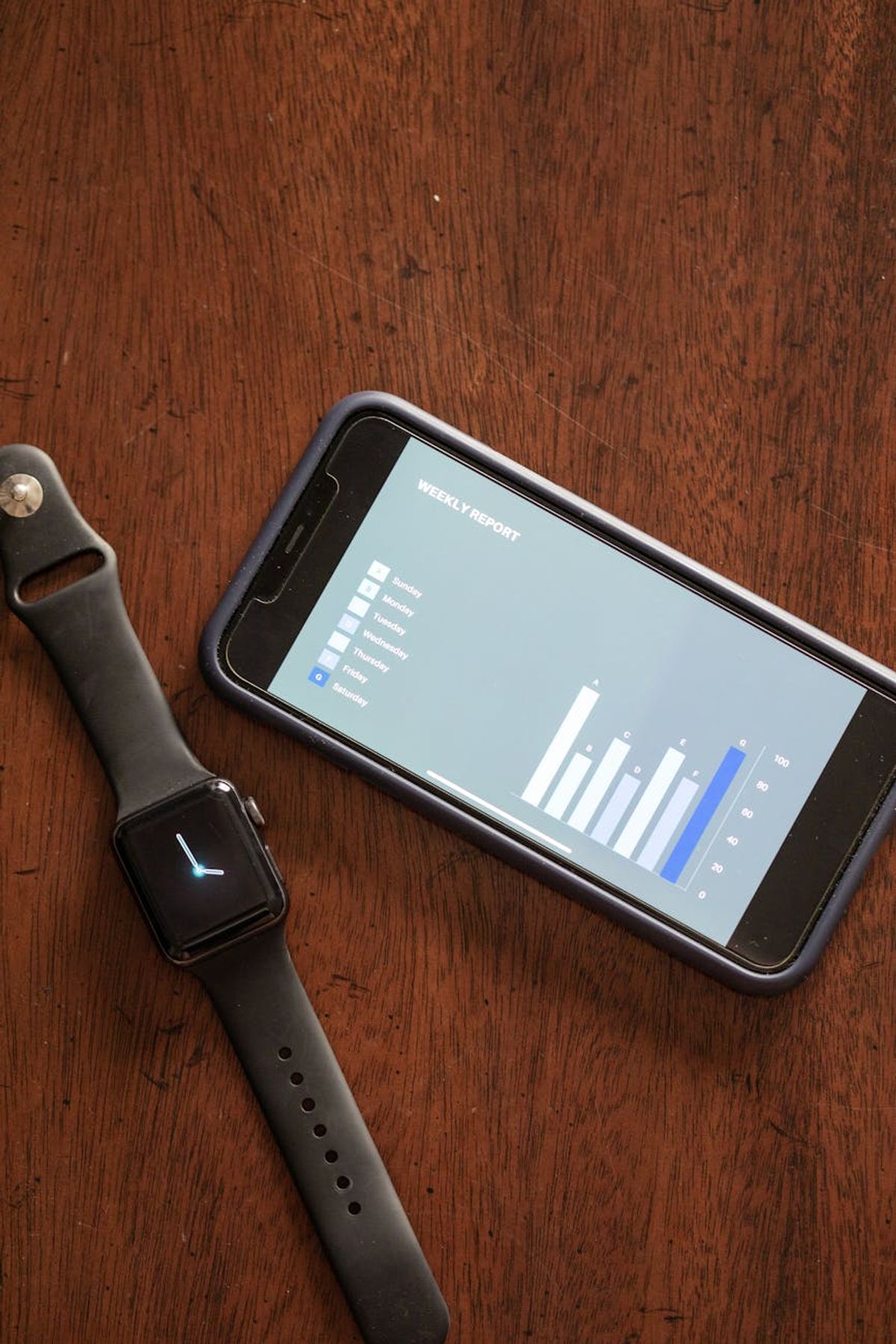 Smartphone and smartwatch displaying data on a wooden table, highlighting technology and analytics.