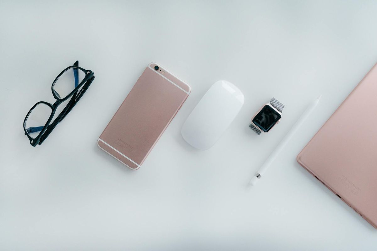 Elegant arrangement of glasses, phone, watch, mouse, pencil, and tablet on a white surface.