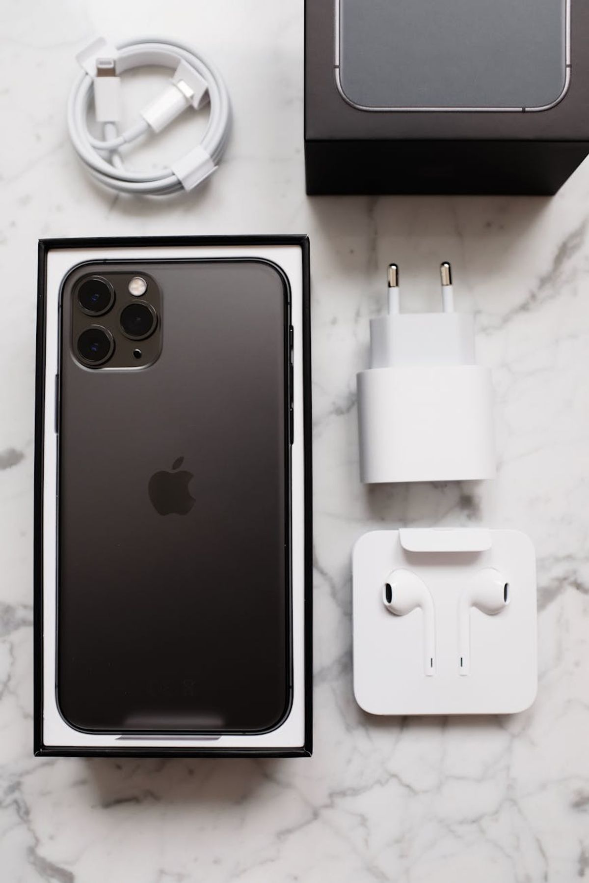 Top view of black smartphone in box package and usb wire for battery charging and wireless earphones on marble table