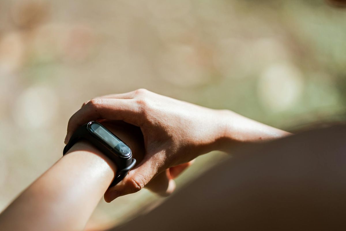 From above of crop anonymous person wearing modern bracelet with small display while standing outdoors on blurred background in daylight
