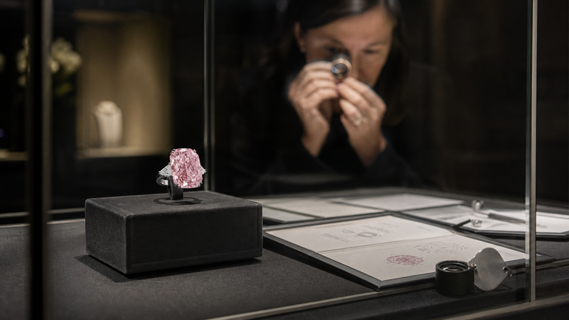 A large pink diamond jewel displayed beside gemological grading documents in a secure gallery