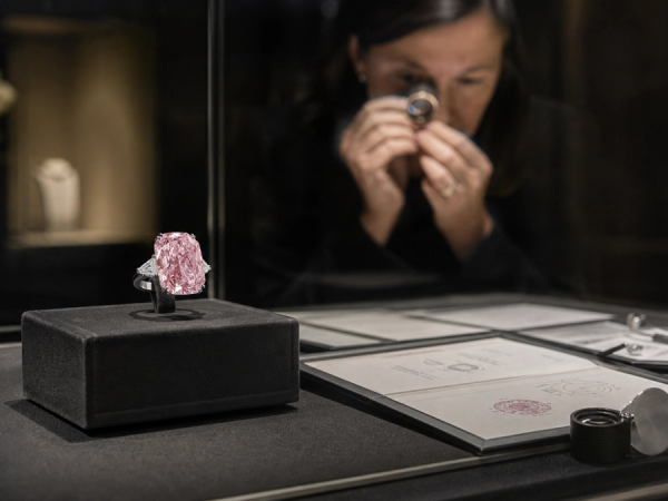 A large pink diamond jewel displayed beside gemological grading documents in a secure gallery