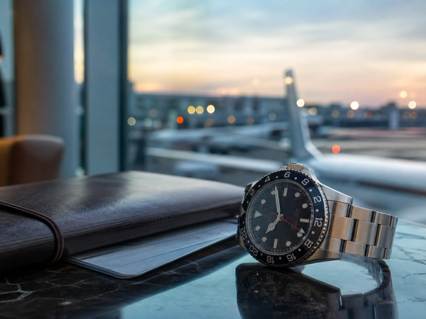 GMT-style mechanical watch beside a travel notebook in an airport lounge at dawn