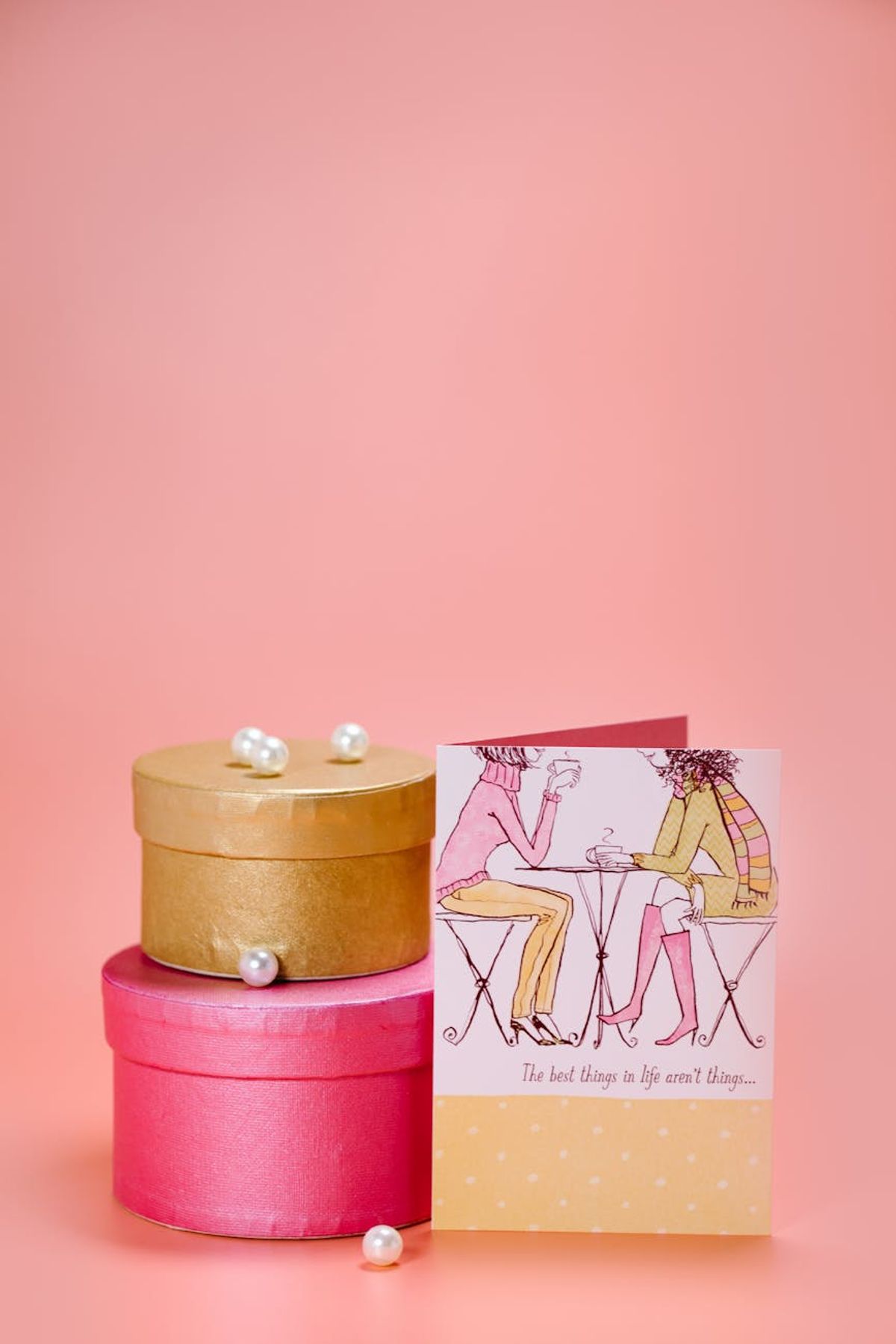 Stacked gift boxes with a greeting card on a pink background, ideal for celebrations.