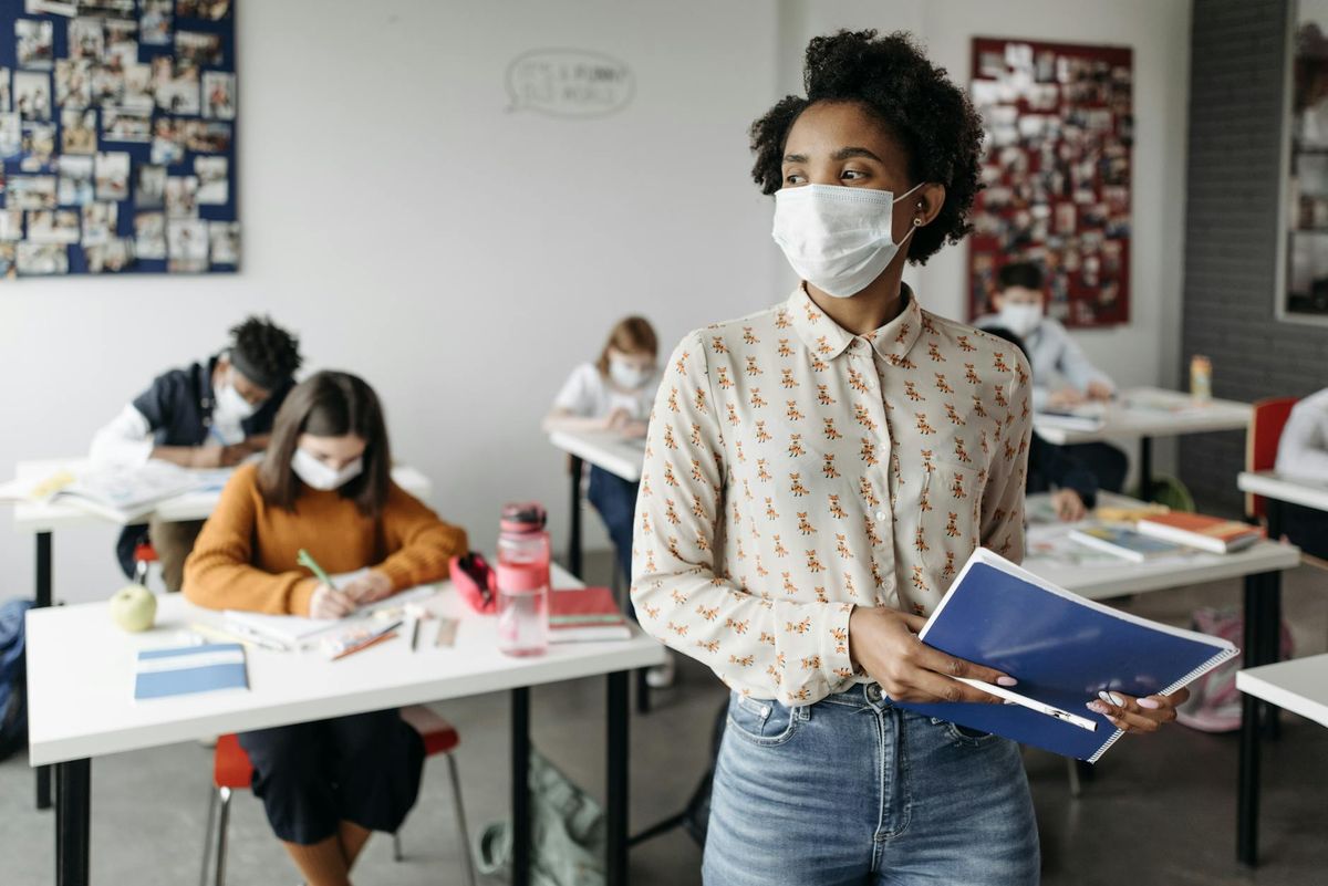 A teacher wearing a mask instructs students in a classroom setting during the pandemic.