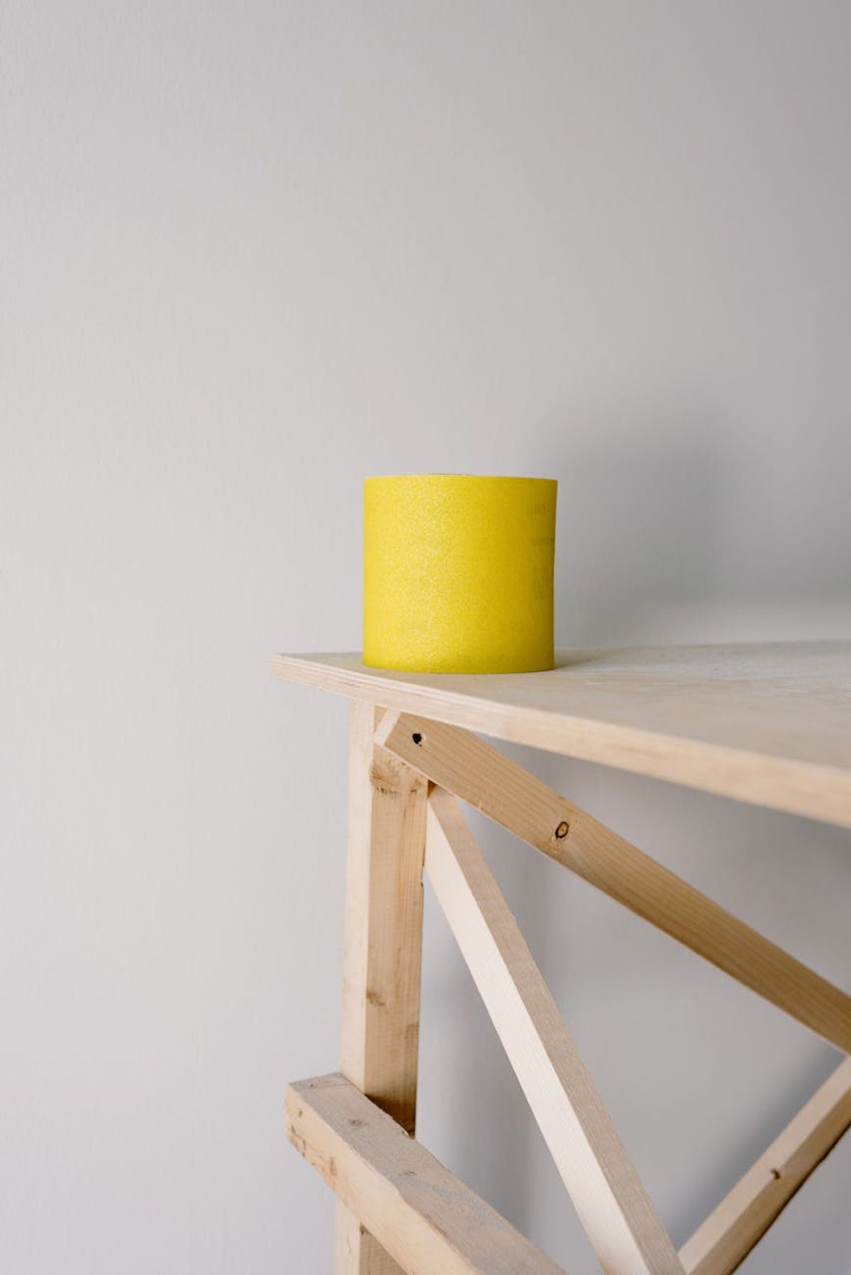 Yellow sandpaper roll placed on wooden scaffold placed in light flat against white wall during renovation