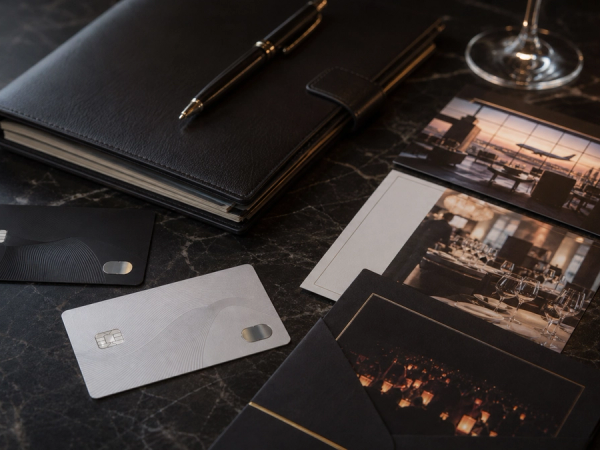 Two distinct unbranded premium payment cards beside a private itinerary folio, airport lounge and curated event invitation