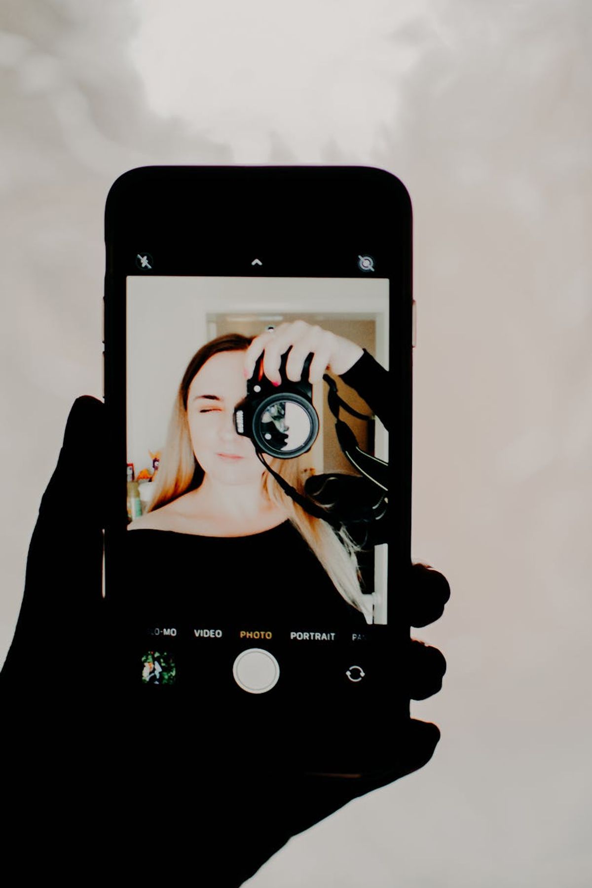 Artistic self-portrait of a woman holding a camera shown on a smartphone screen.