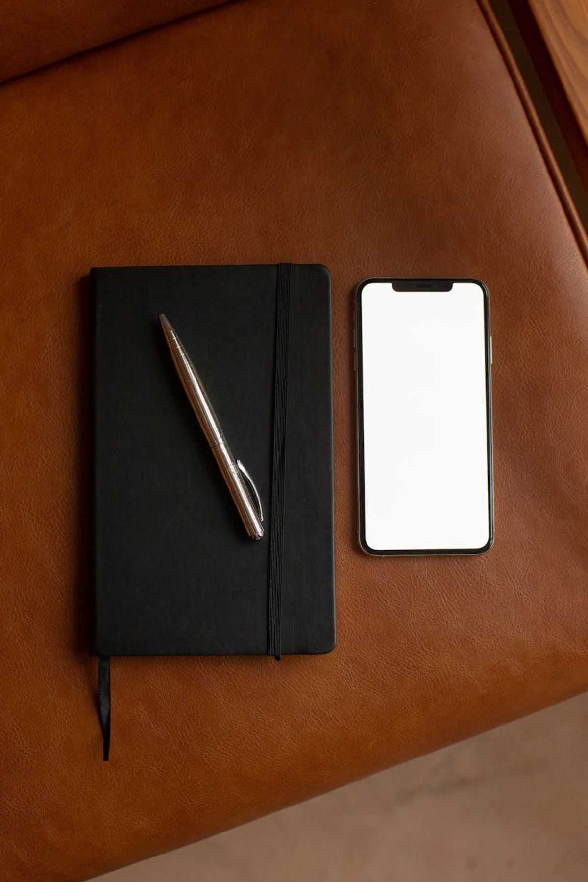 A top-down view of a notebook, ballpen, and smartphone on a leather surface.
