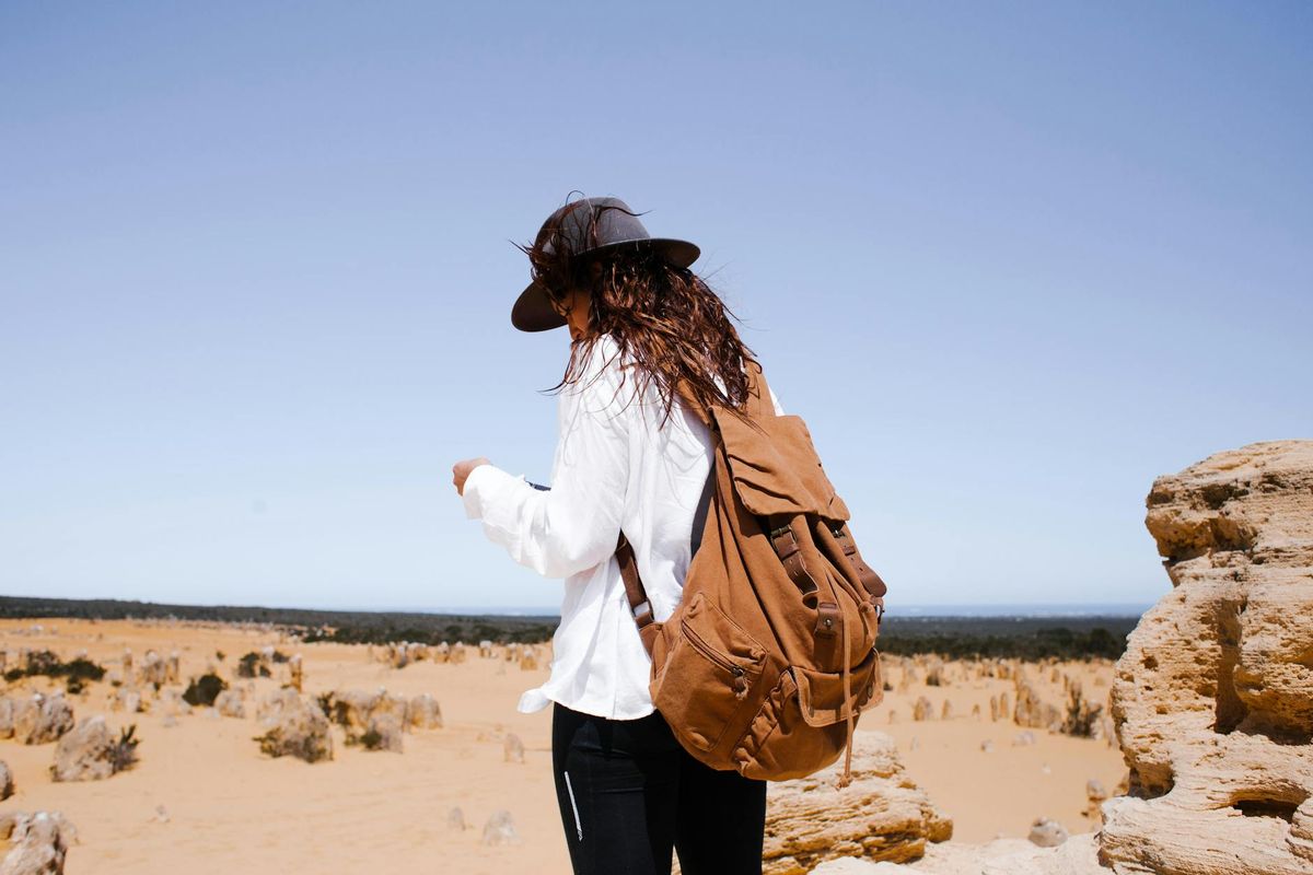 A woman wearing a hat and backpack explores a remote desert landscape under a clear blue sky.