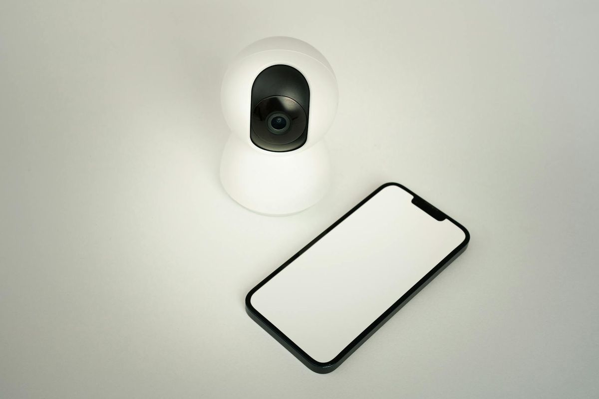 A smart home security camera paired with a blank smartphone on a white background.