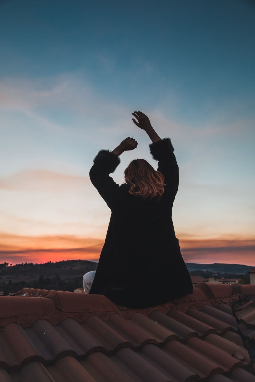 A woman on a rooftop overlooking the hills at sunset