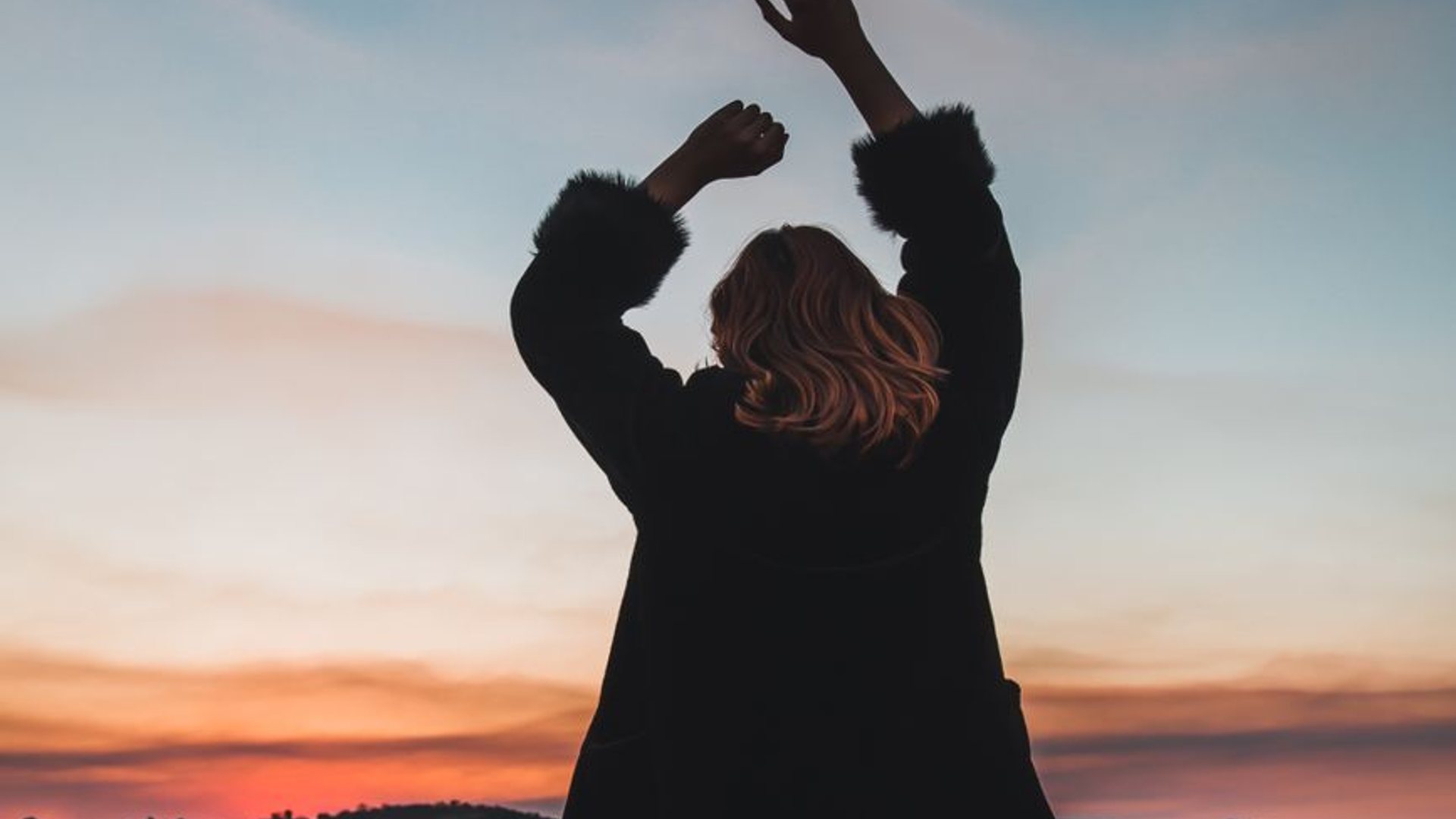 A woman on a rooftop overlooking the hills at sunset
