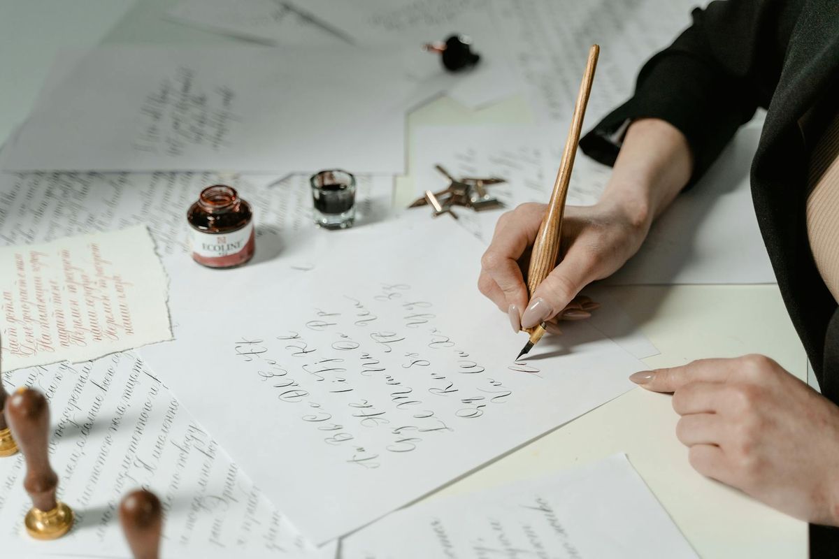 Close-up of an adult writing calligraphy with a fountain pen on a table.