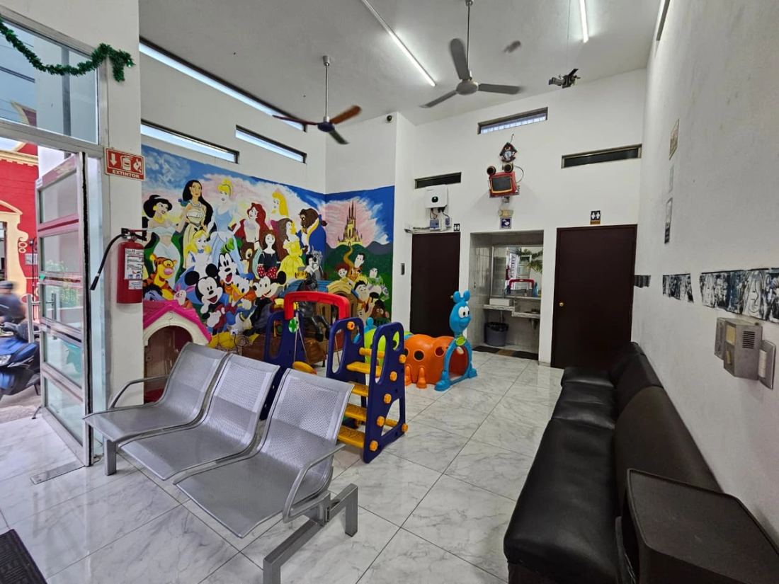 Área infantil vista desde la entrada, con los juegos, las sillas de espera y el sillón