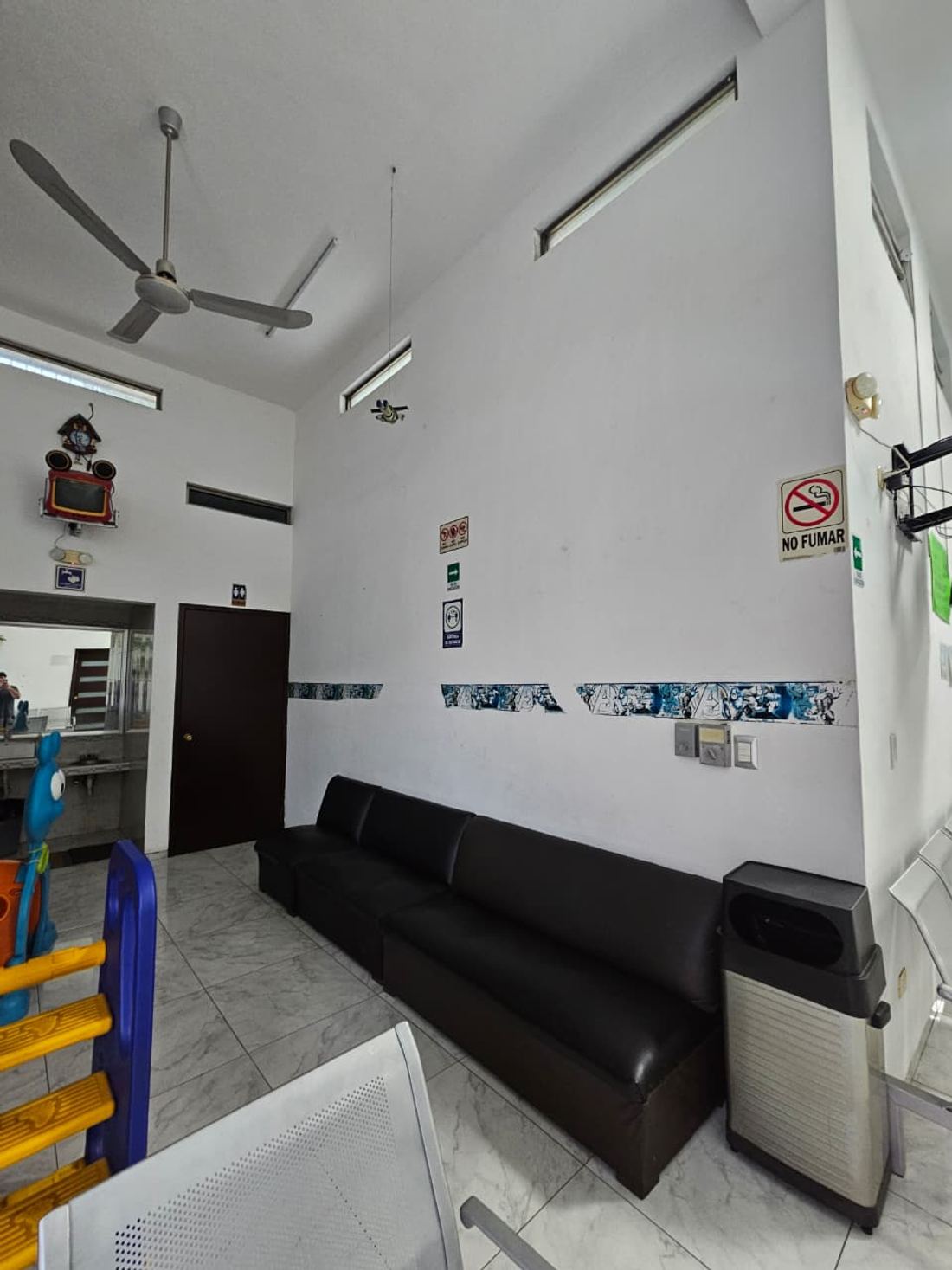 Sala de espera con sillón largo y sillas metálicas, junto al área infantil