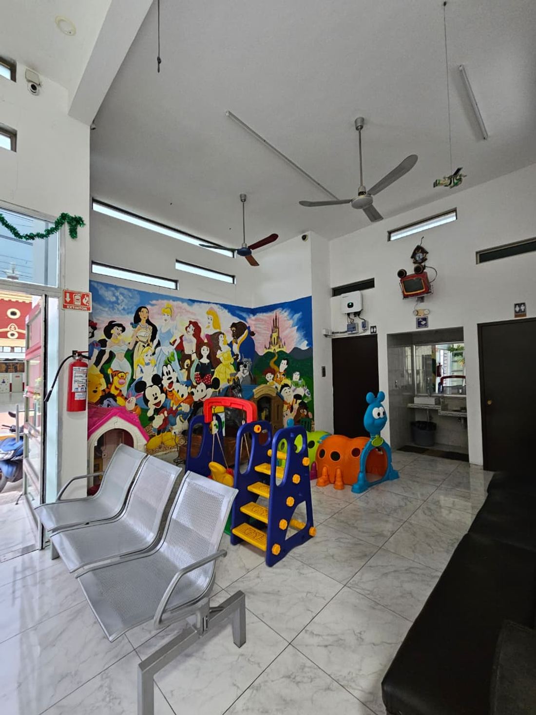 Rincón de juegos infantil junto a la entrada de la clínica, con el mural al fondo