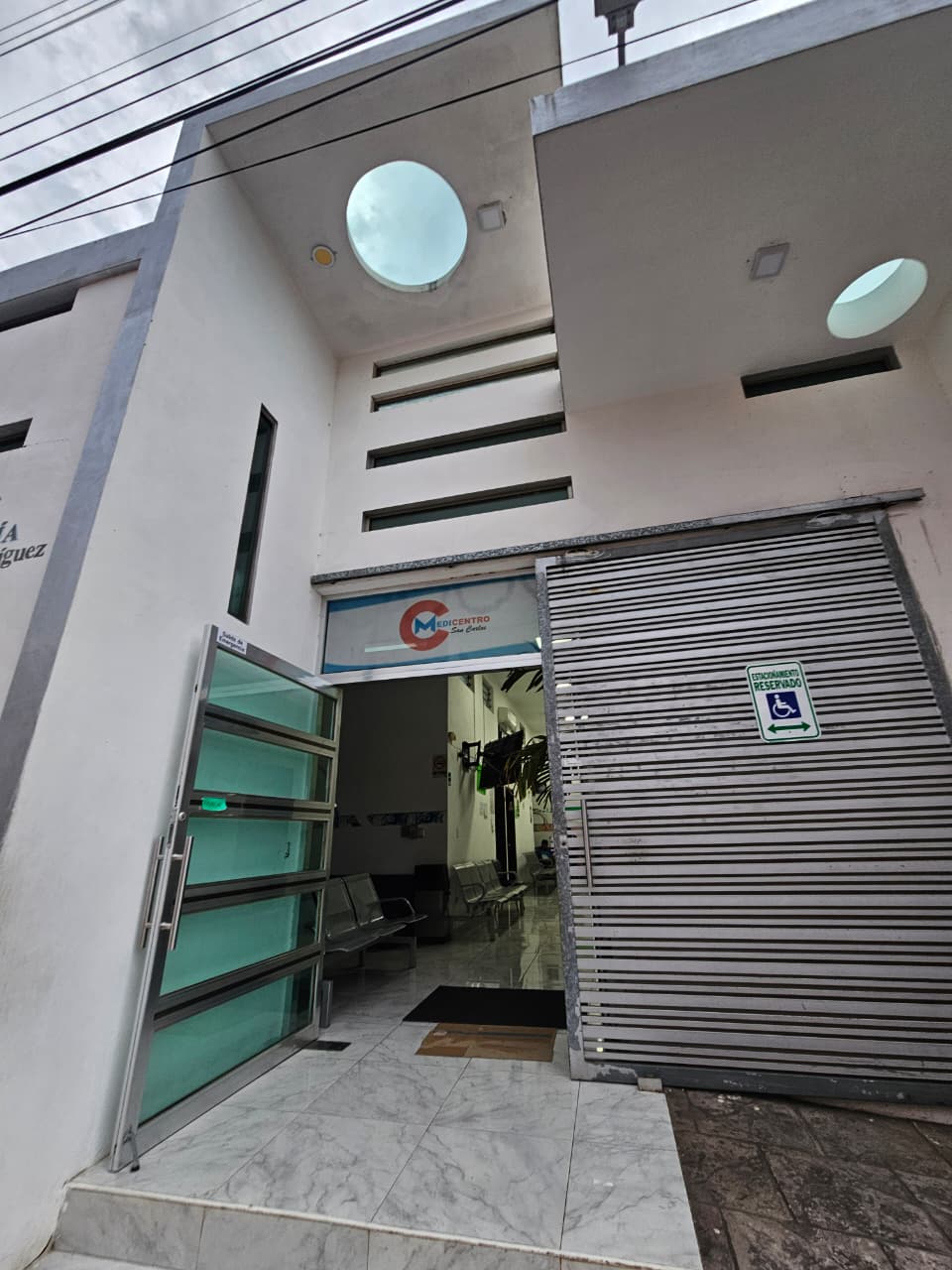 Entrada principal de MEDICENTRO San Carlos con la puerta de cristal abierta y el cajón de estacionamiento reservado