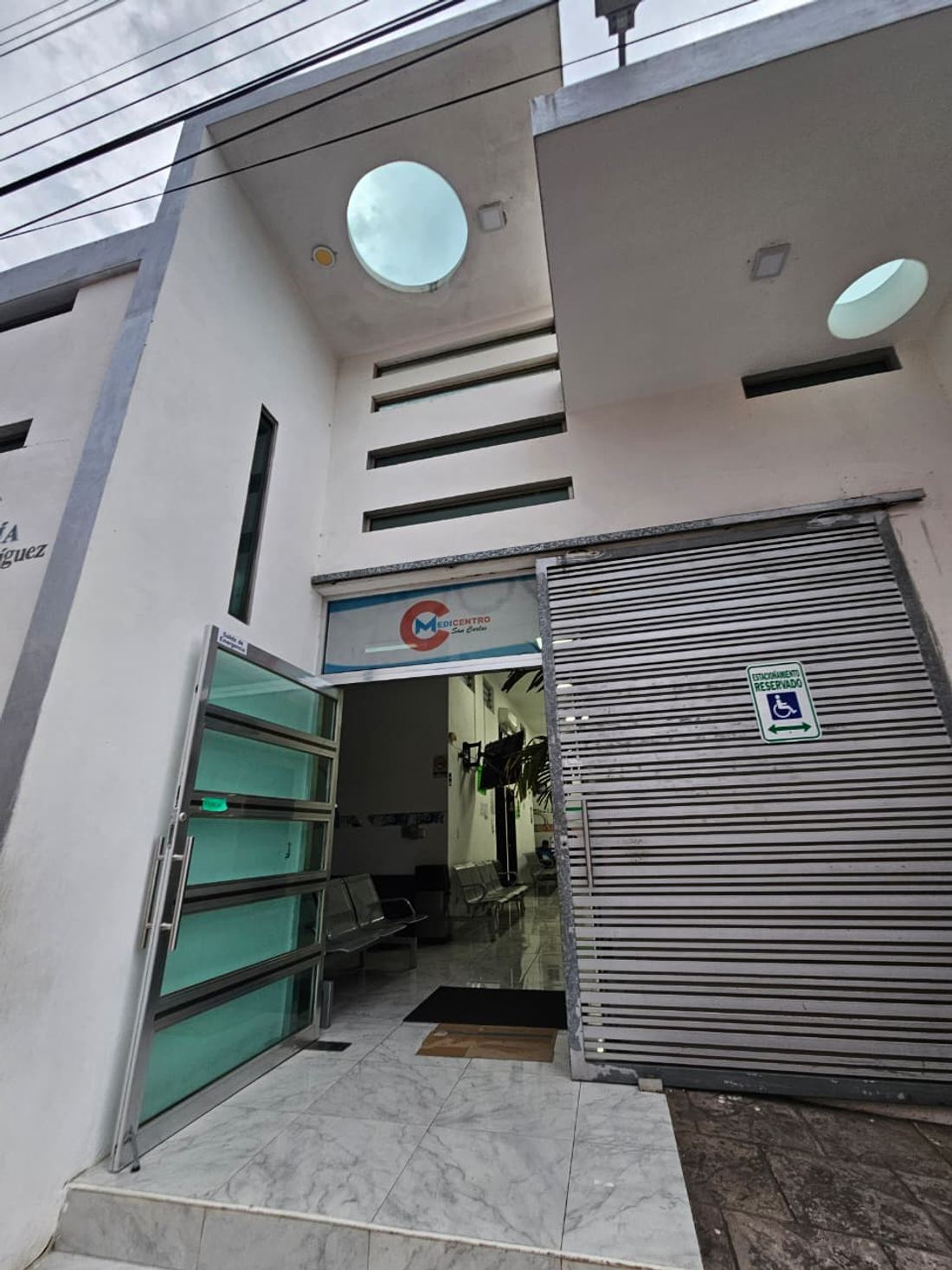 Entrada principal de MEDICENTRO San Carlos con la puerta de cristal abierta y el cajón de estacionamiento reservado