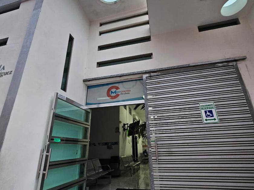 Entrada principal de MEDICENTRO San Carlos con la puerta de cristal abierta y el cajón de estacionamiento reservado