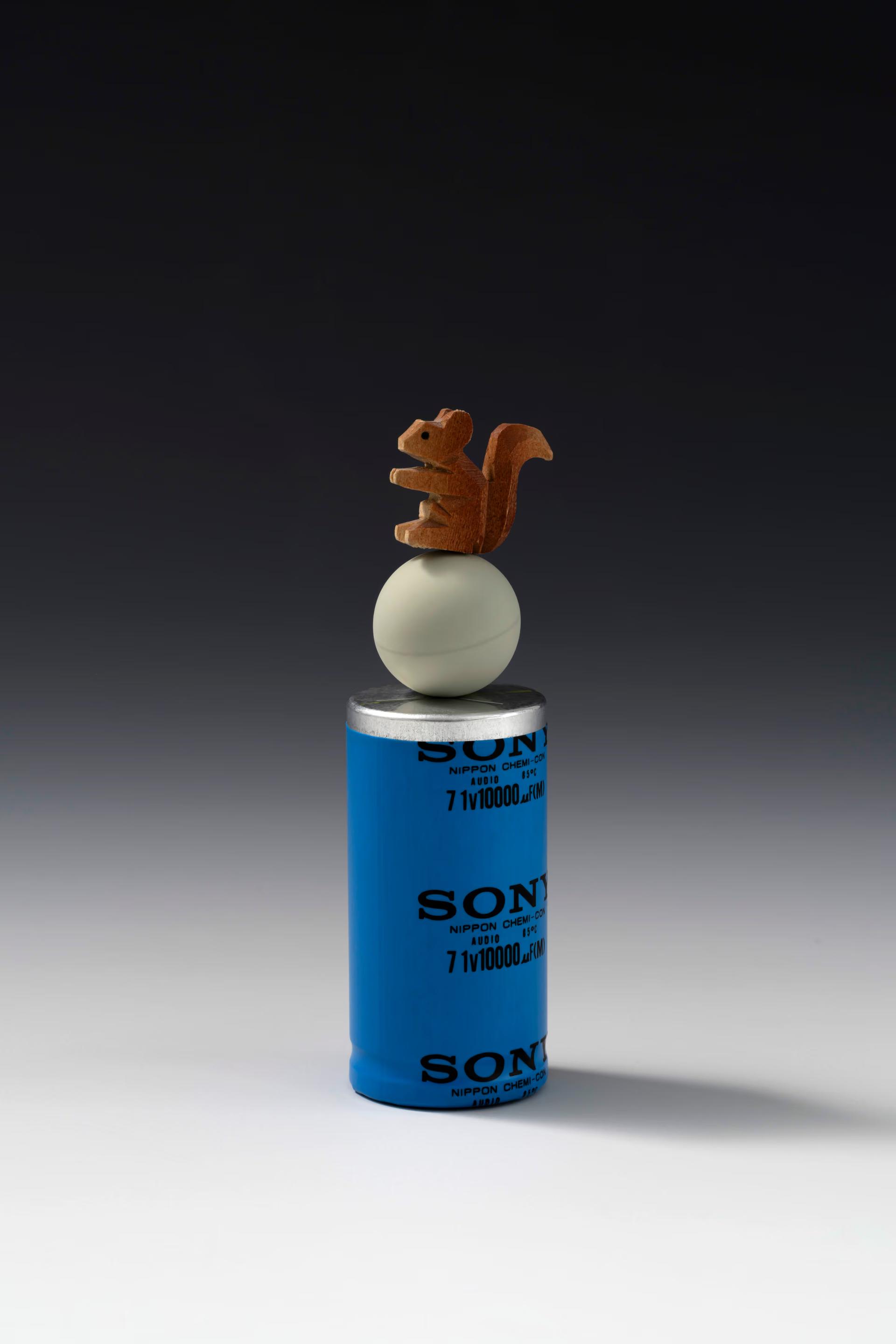 Squirrel sculpture balanced above a blue cylinder