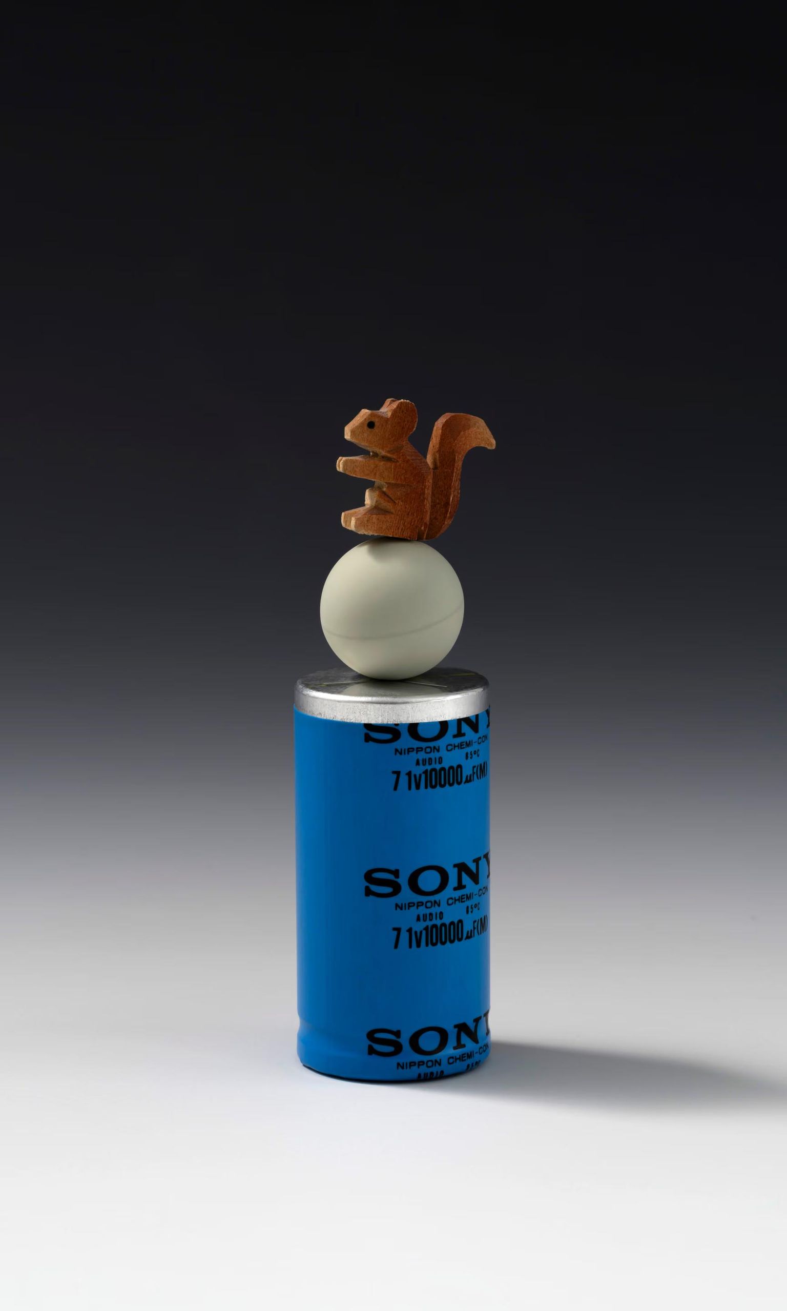 Squirrel sculpture balanced above a blue cylinder