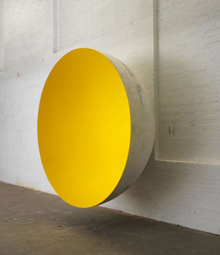 Yellow circular sculpture in a brick-walled gallery