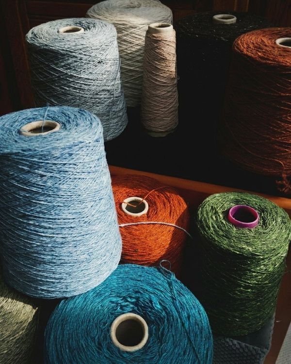 Stożki przędzy Donegal z wełny merino w różnych naturalnych kolorach. Charakterystyczne kolorowe nepsy i miękka przędza przygotowana do ręcznego tkania szali oraz tekstyliów