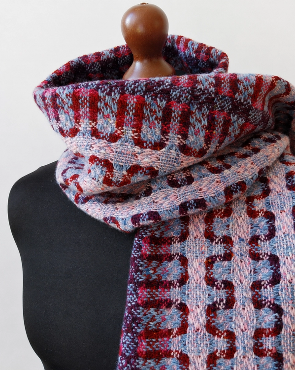 Handwoven merino wool scarf in shades of red, purple, pink and blue, featuring a reversible textured pattern.