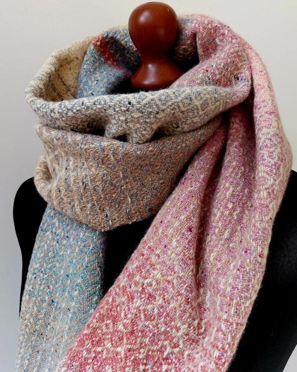 Handwoven scarf woven on a floor loom from natural Donegal merino wool, shown from both sides. Geometric patterns in pastel blue, pink and cream reveal the reversible character of this artisan woven textile.
