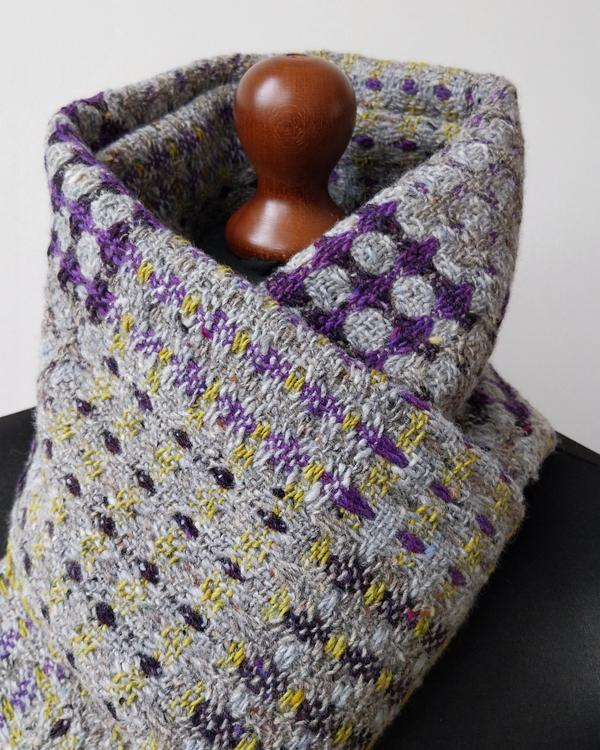 Handwoven merino wool scarf featuring a geometric pattern in grey, purple, and yellow.