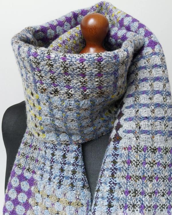 Handwoven merino wool scarf featuring a geometric pattern in grey, purple, and yellow.