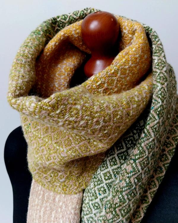 Handwoven artisan scarf made from Irish Donegal merino wool in shades of ecru, olive green and warm yellow. The soft natural woven textile with a subtle geometric texture is displayed on a black dress form.