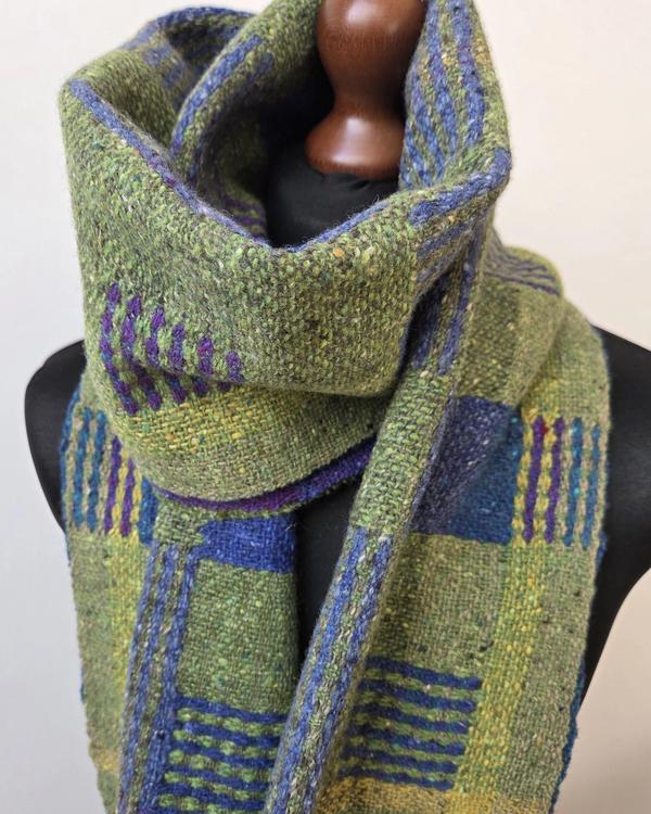 Handwoven scarf in shades of green, blue, purple and yellow, softly draped on a mannequin.