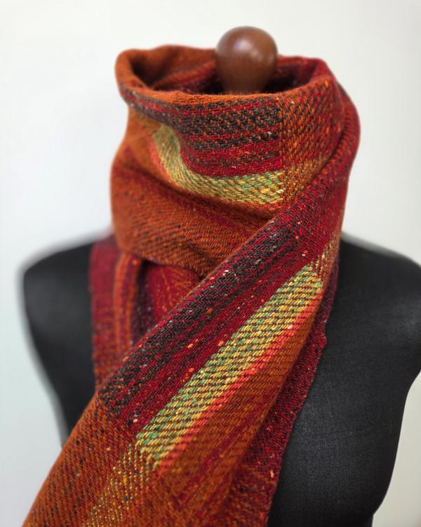 Handwoven merino wool scarf in vivid shades of red, orange, ochre and green, arranged on a black mannequin.