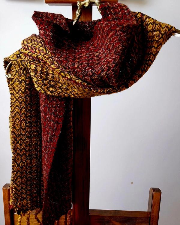 Handwoven merino wool scarf “Autumn Leaves” featuring rich burgundy, red, gold and brown tones. Artisan woven winter scarf with geometric texture and warm autumn-inspired colours