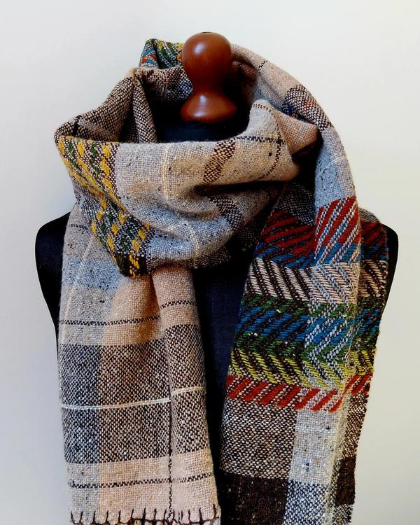 Handwoven Donegal wool shawl in beige, grey, blue, green and rust-orange tones displayed on a mannequin. Long artisan shawl inspired by landscape colours and woven textures.