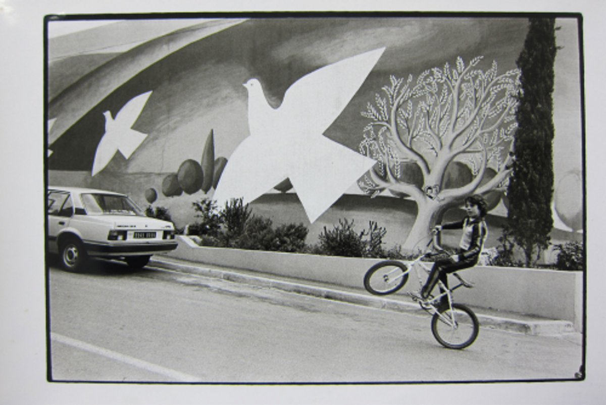 Jean Dieuzaide, Garçon à vélo devant le supermarché Sodim au mur peint d’un paysage avec des colombes, rue des Arbousiers, Carros, avril 1983, tirage gélatino-argentique. © Jean Dieuzaide/ Les Arts Décoratifs