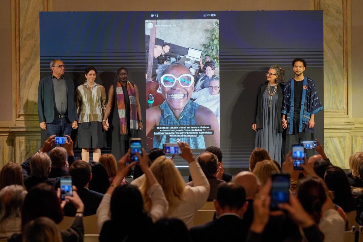 Gabe Beckhurst Feijoo, Marie Hélène Pereira, Rasha Salti, Siddhartha Mitter et Rory Tsapayi entourent une capture d'écran du compte Instagram de la défunte commissaire Koyo Kouoh lors de la présentation de La Biennale Arte 2026 à la Ca’Giustinian, siège de la Biennale à Venise, le 27 mai 2025. Photo : Andrea Avezzù. Courtesy de La Biennale di Venezia