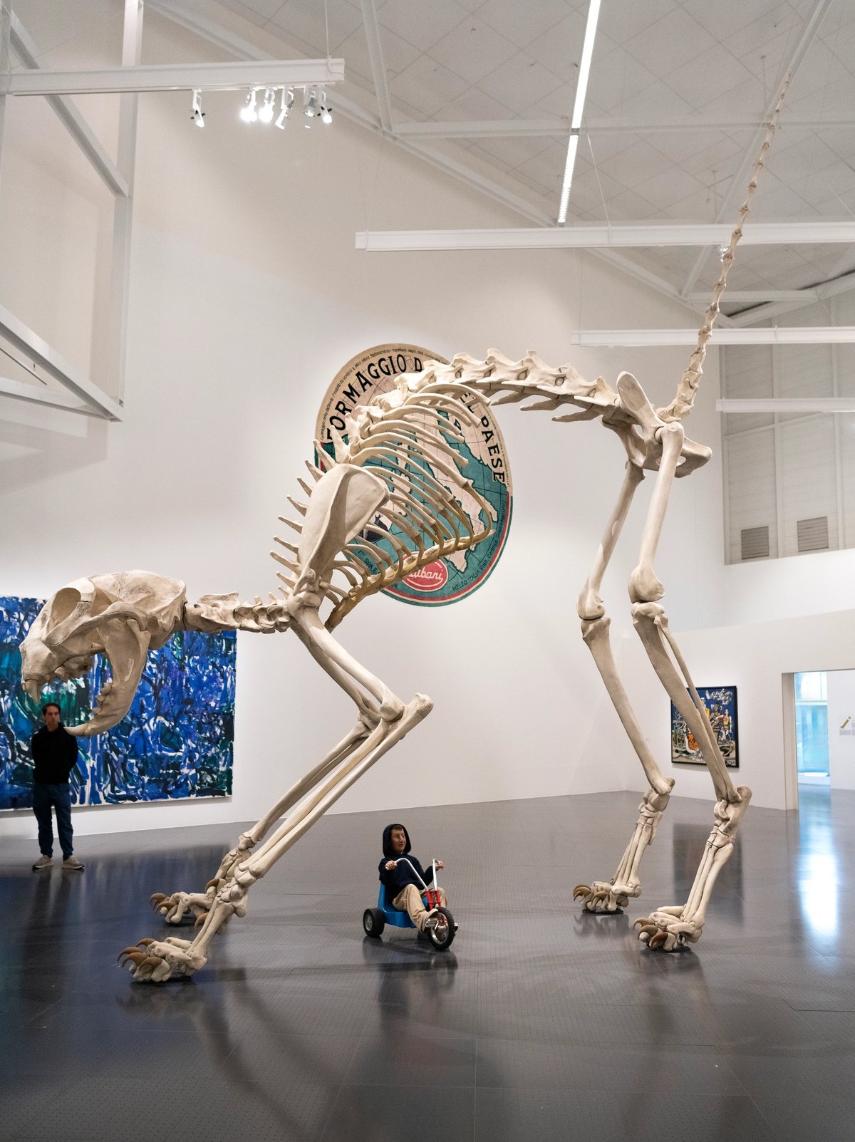 Vue de l’exposition « Dimanche sans fin » : Felix (2001, huile sur polyvinyle, résine et fibre de verre) et Charlie (2003, tricycle, acier, vernis, gomme, résine, silicone, cheveux naturels, tissus, pile et télécommande), Centre Pompidou-Metz, 2025. Courtesy des Maurizio Cattelan’s Archive. Photo Centre Pompidou-Metz/Marc Domage