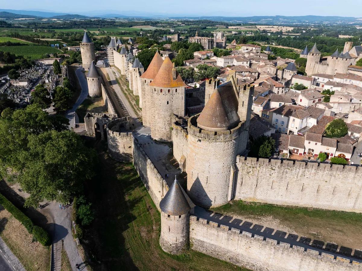 Vue aérienne de la cité médiévale de Carcassonne, dans le département de l’Aude. Grâce à un projet de restauration de l’enceinte et des tours de guet, les visiteurs peuvent désormais parcourir un circuit complet de 1,3 kilomètre sur les remparts supérieurs. © Sammy Billon – CMN